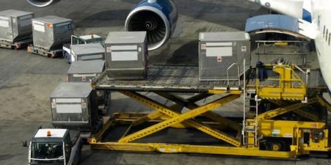 Air cargo containers on a scissor-lift loader being loaded into an aircraft beside a jet engine on the tarmac.