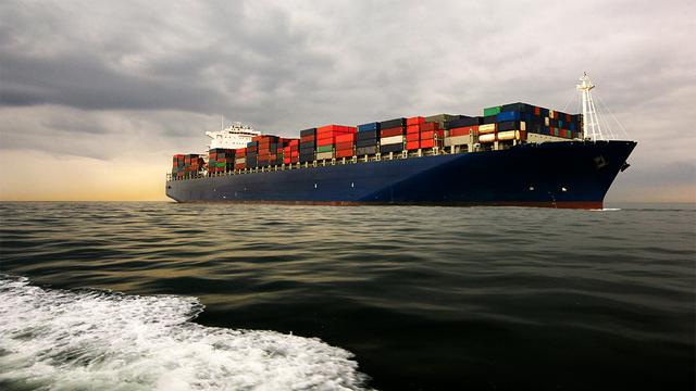 Large container ship loaded with stacked containers sailing on open sea under a cloudy golden sky