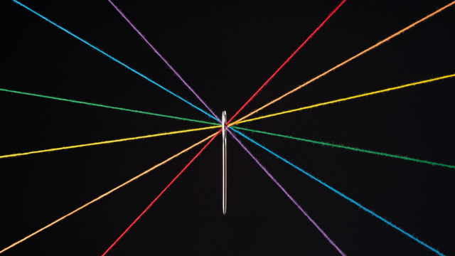 Thin multicolored lines radiating from a single central point on a black background, like converging light beams.