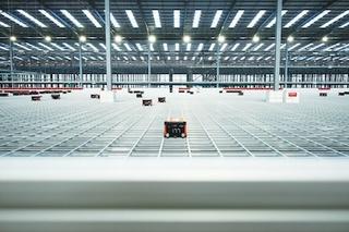 Photo of a large fulfillment warehouse interior with an automated storage grid and robotic units moving across it.