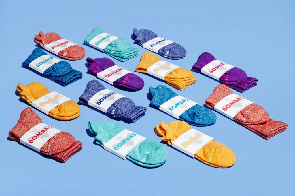 Rows of packaged Bombas socks in assorted colors arranged on a light blue background