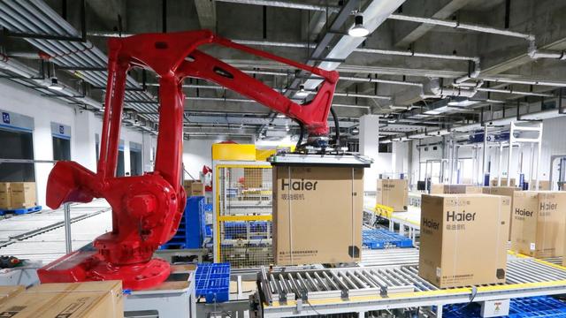 Red industrial robotic arm moving Haier-branded boxes along conveyor rollers in an automated warehouse
