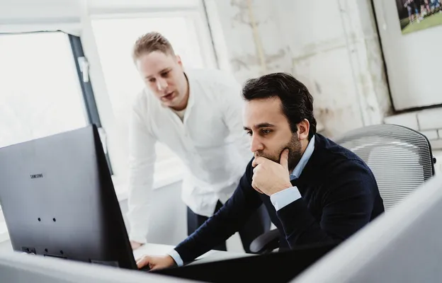 Close-up van een professional die op een toetsenbord typt naast een laptop in een moderne werkruimte, wat productiviteit, technologie en digitale werkomgevingen symboliseert.