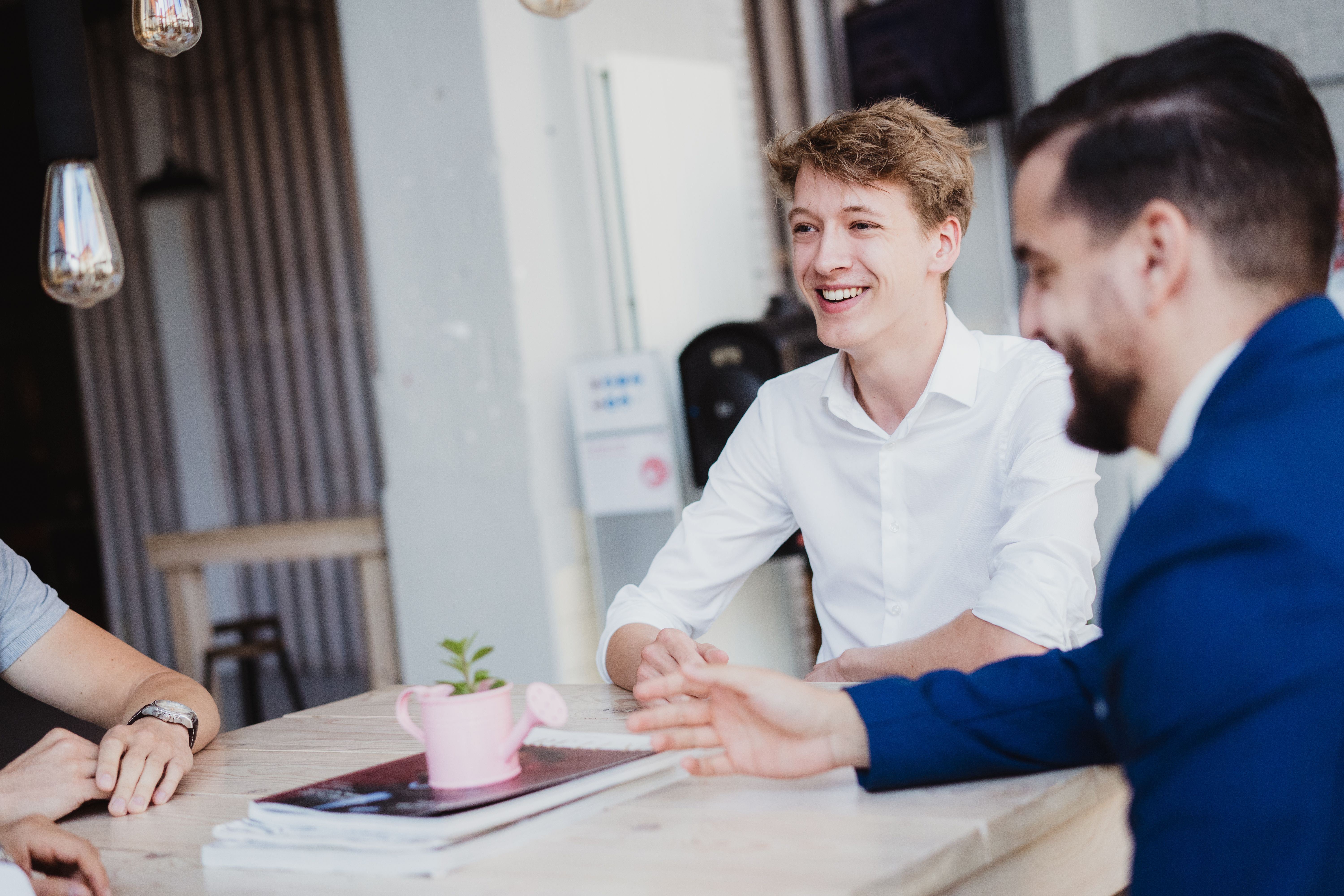 Een groep professionals zit in een lichte, moderne vergaderruimte rond een tafel te overleggen, wat wijst op een gezamenlijk zakelijk gesprek of een teamvergadering.