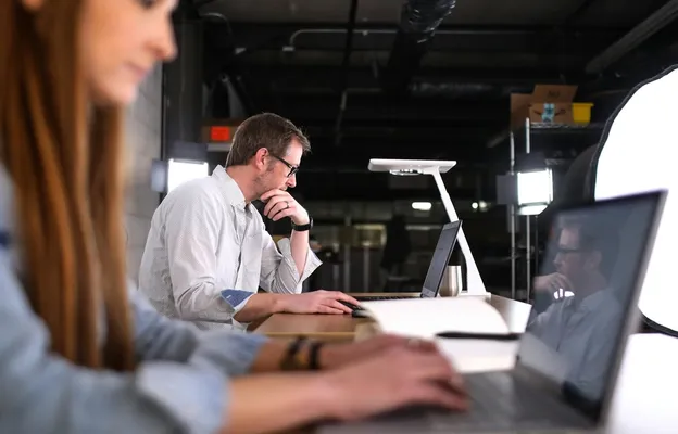 Een professionele man met een bril kijkt geconcentreerd naar zijn laptop in een moderne studio-omgeving; symbool voor de transparante en zorgvuldige aard van moderne EU-wervingsprocessen