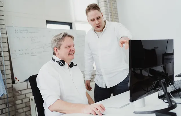 Two men discussing work at a desktop computer in a modern office