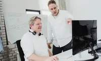 Two men discussing work at a desktop computer in a modern office