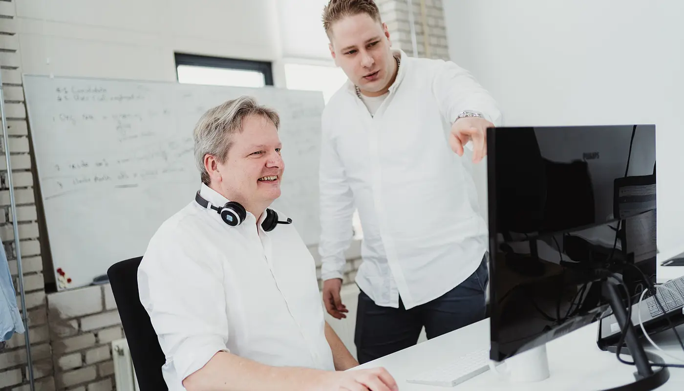 Two men discussing work at a desktop computer in a modern office