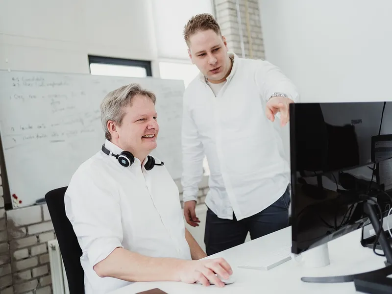 Two men discussing work at a desktop computer in a modern office