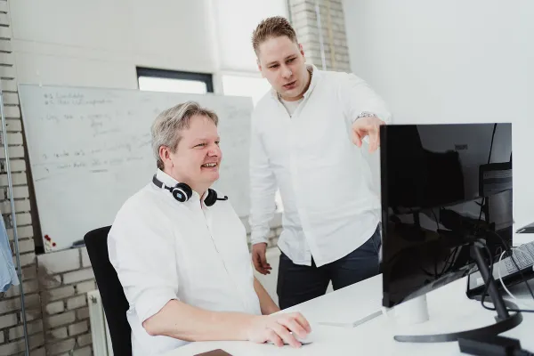 Two men discussing work at a desktop computer in a modern office