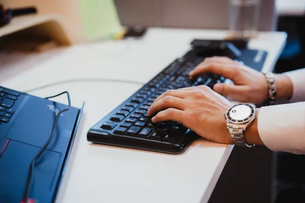 Close-up van een professional die op een toetsenbord typt naast een laptop in een moderne werkruimte, wat productiviteit, technologie en digitale werkomgevingen symboliseert.
