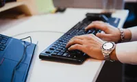 Close-up of a professional typing on a keyboard next to a laptop in a modern workspace, representing productivity, technology, and digital work environments.