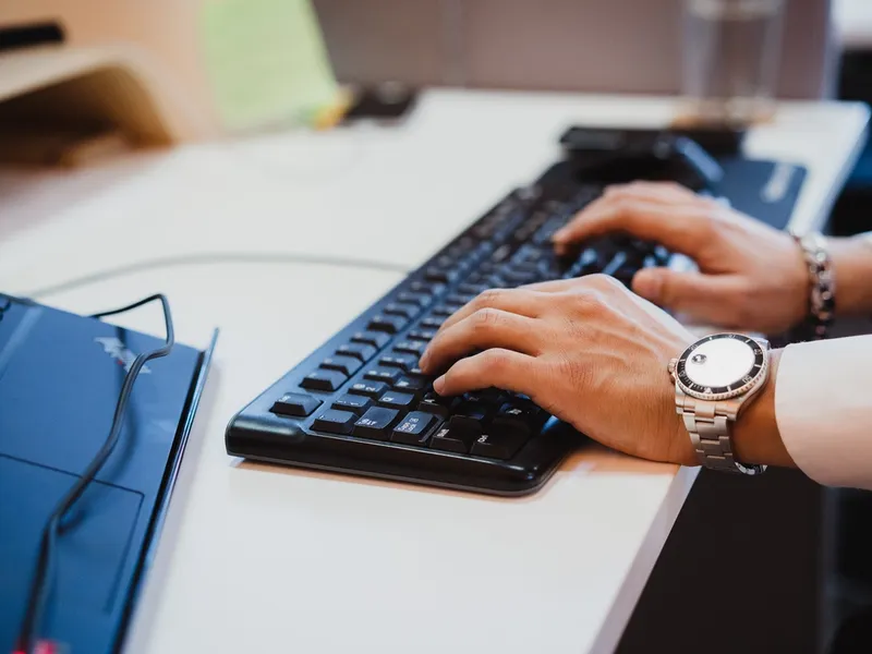 Close-up van een professional die op een toetsenbord typt naast een laptop in een moderne werkruimte, wat productiviteit, technologie en digitale werkomgevingen symboliseert.