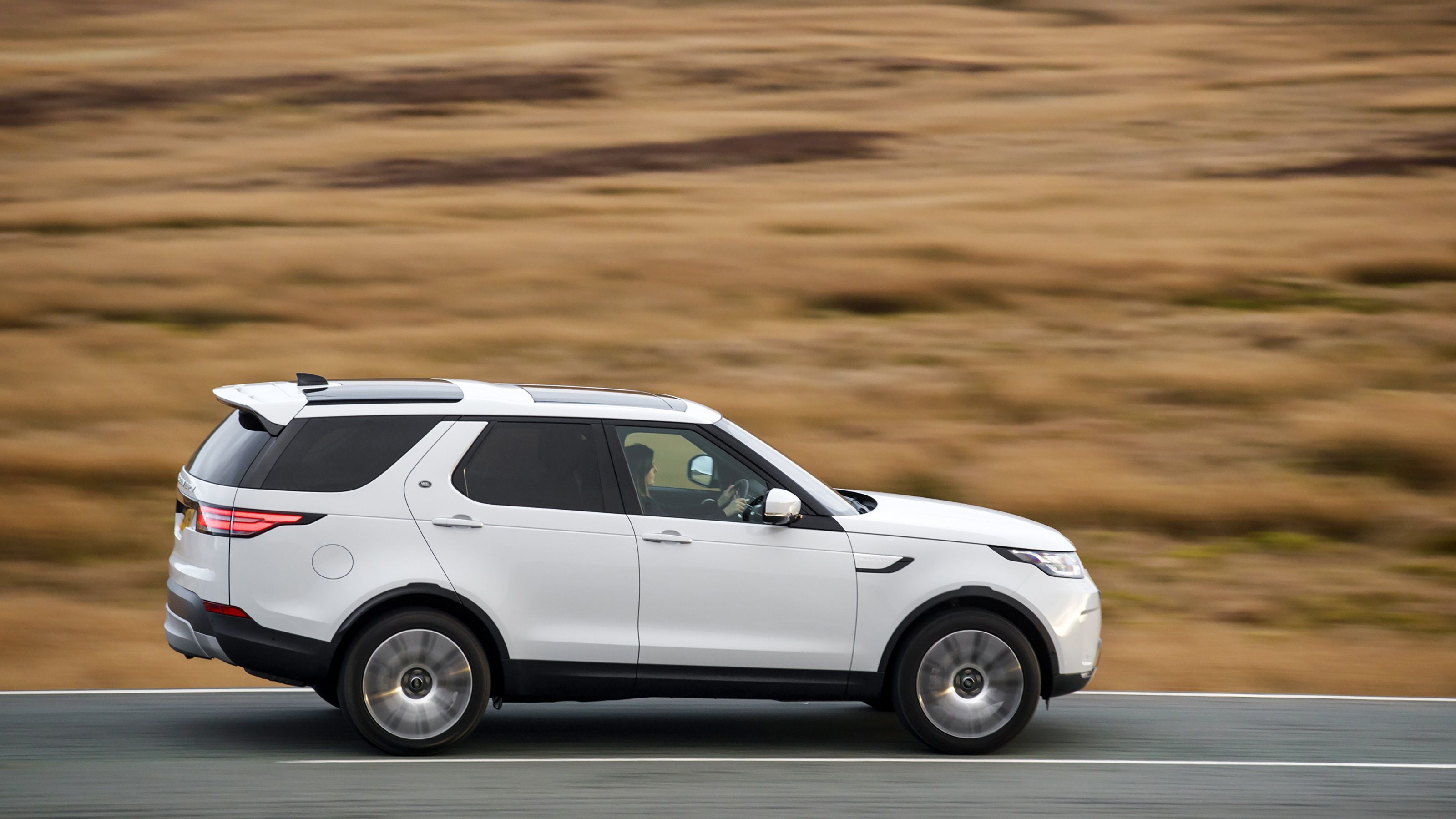 White Land Rover Discovery side driving