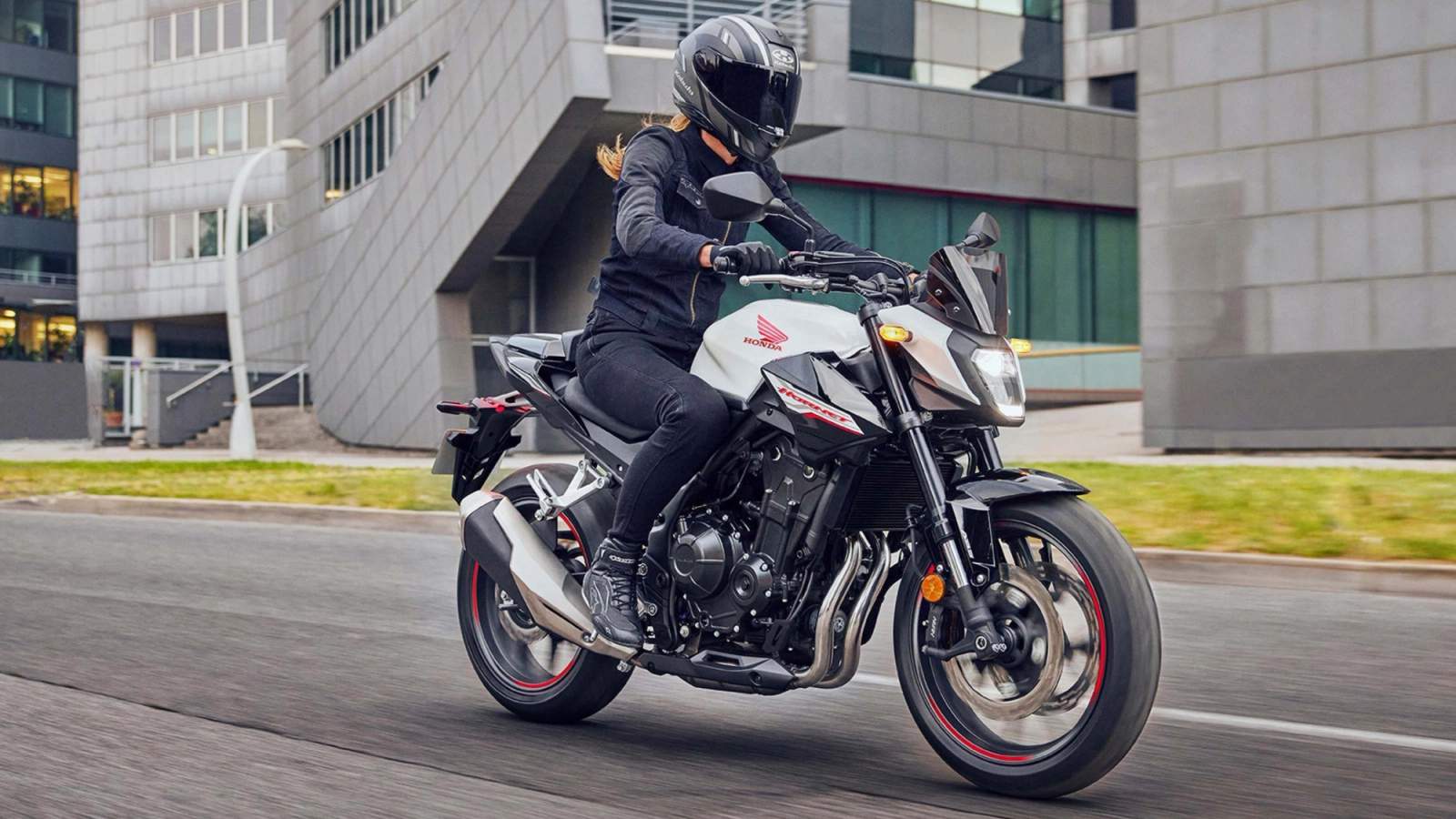 Honda CB500 being ridden beside large buildings