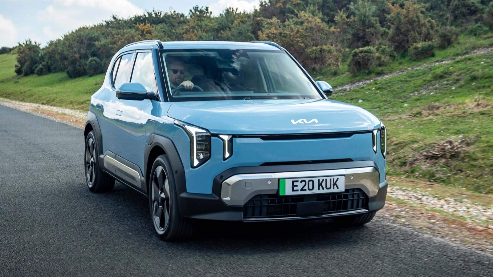 Blue Kia EV2 driving on a country road