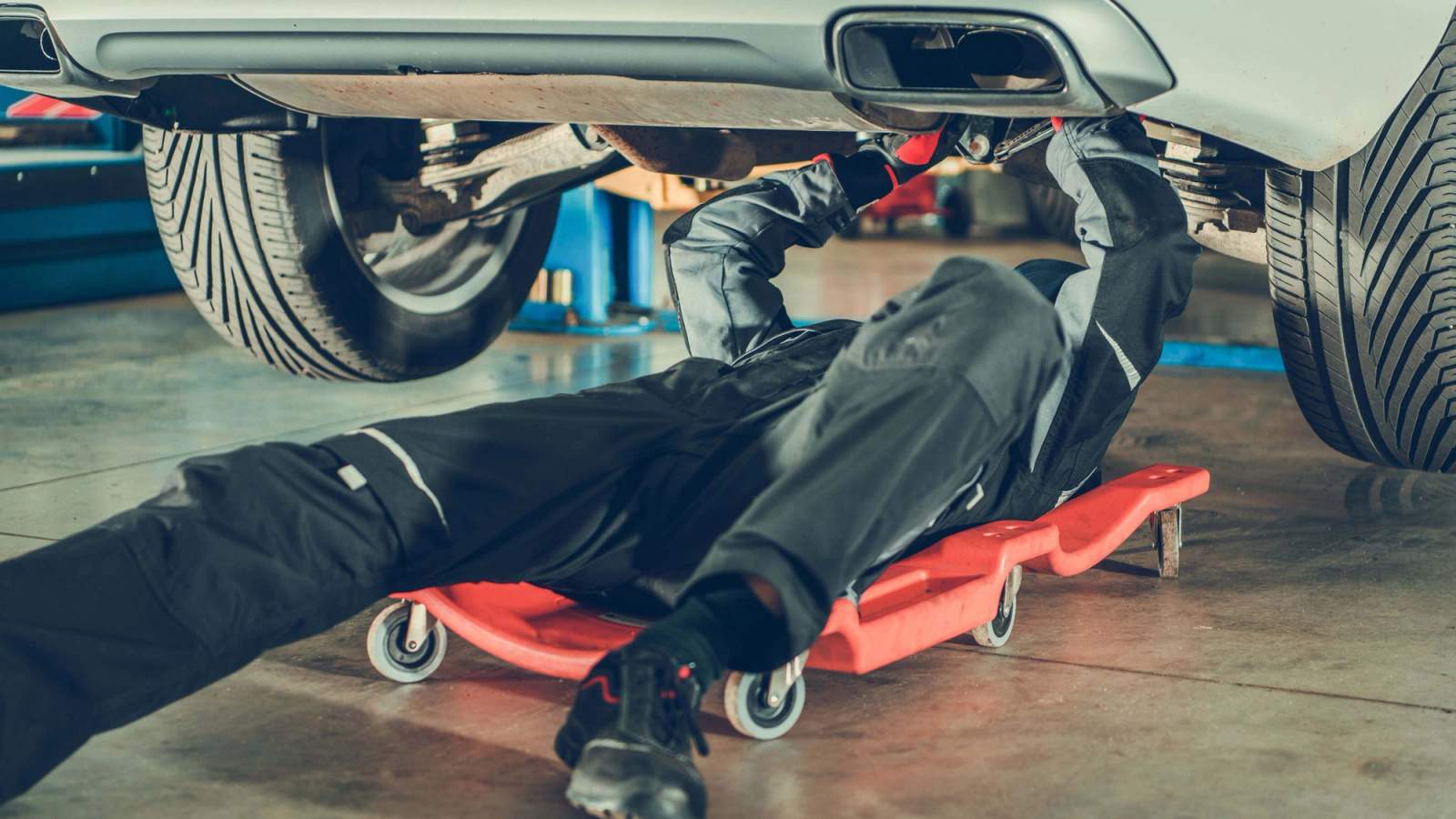 A mechanic inspecting the underside of a car for pothole damage