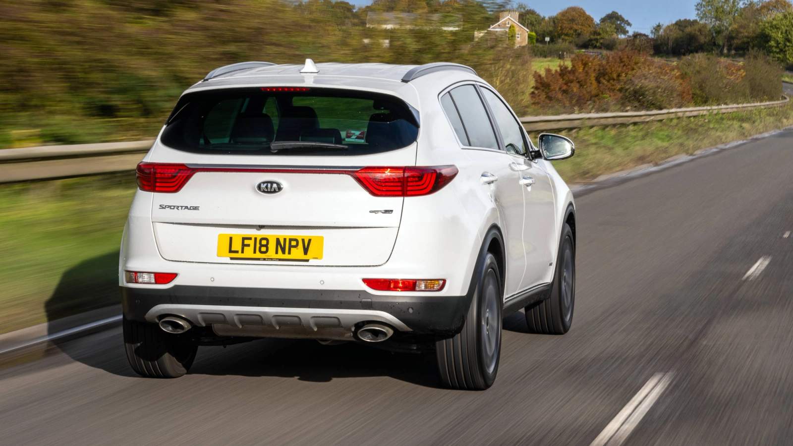 White Kia Sportage driving on a country road