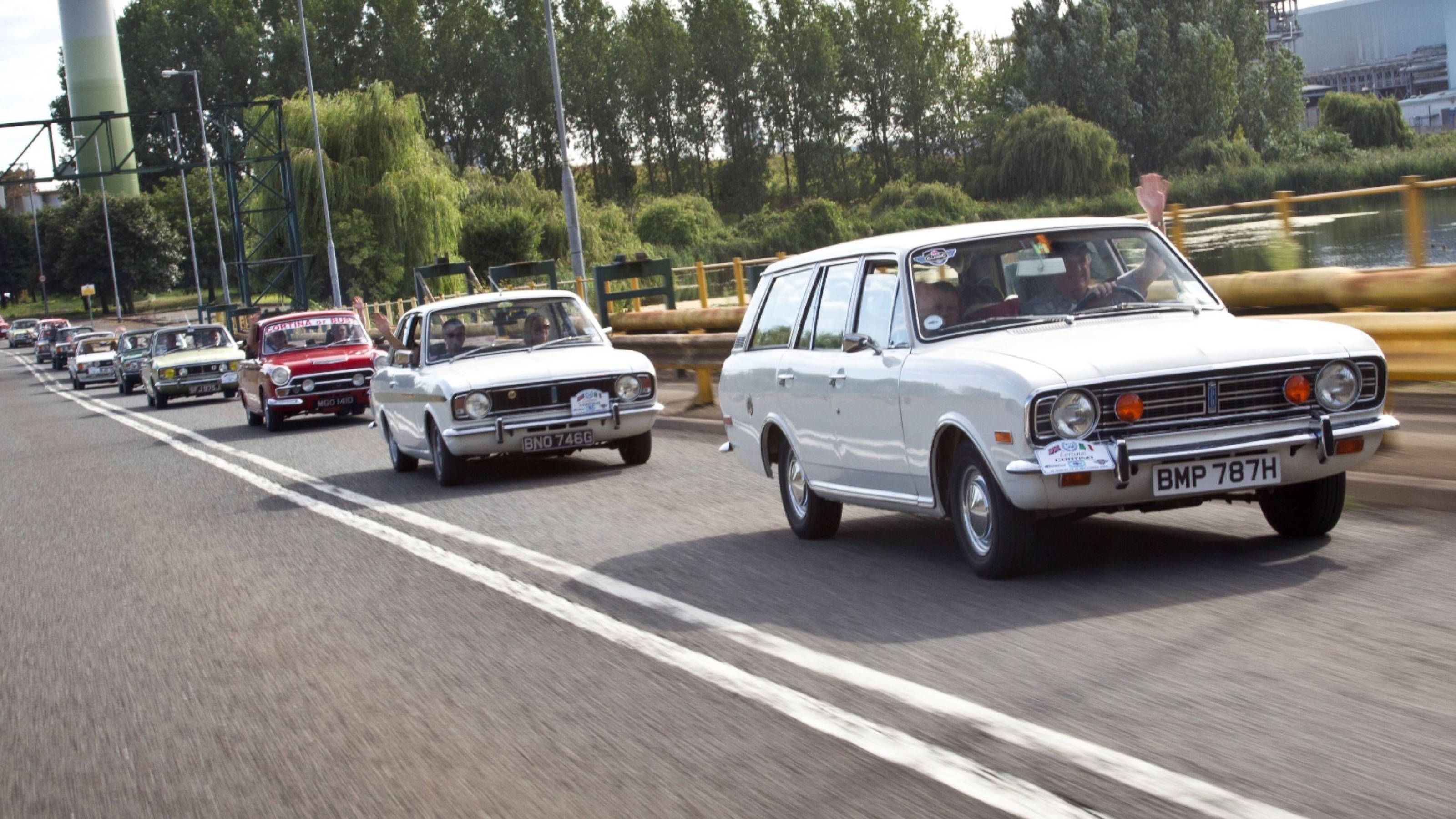 A convoy of classic Ford Cortina models driving along a road