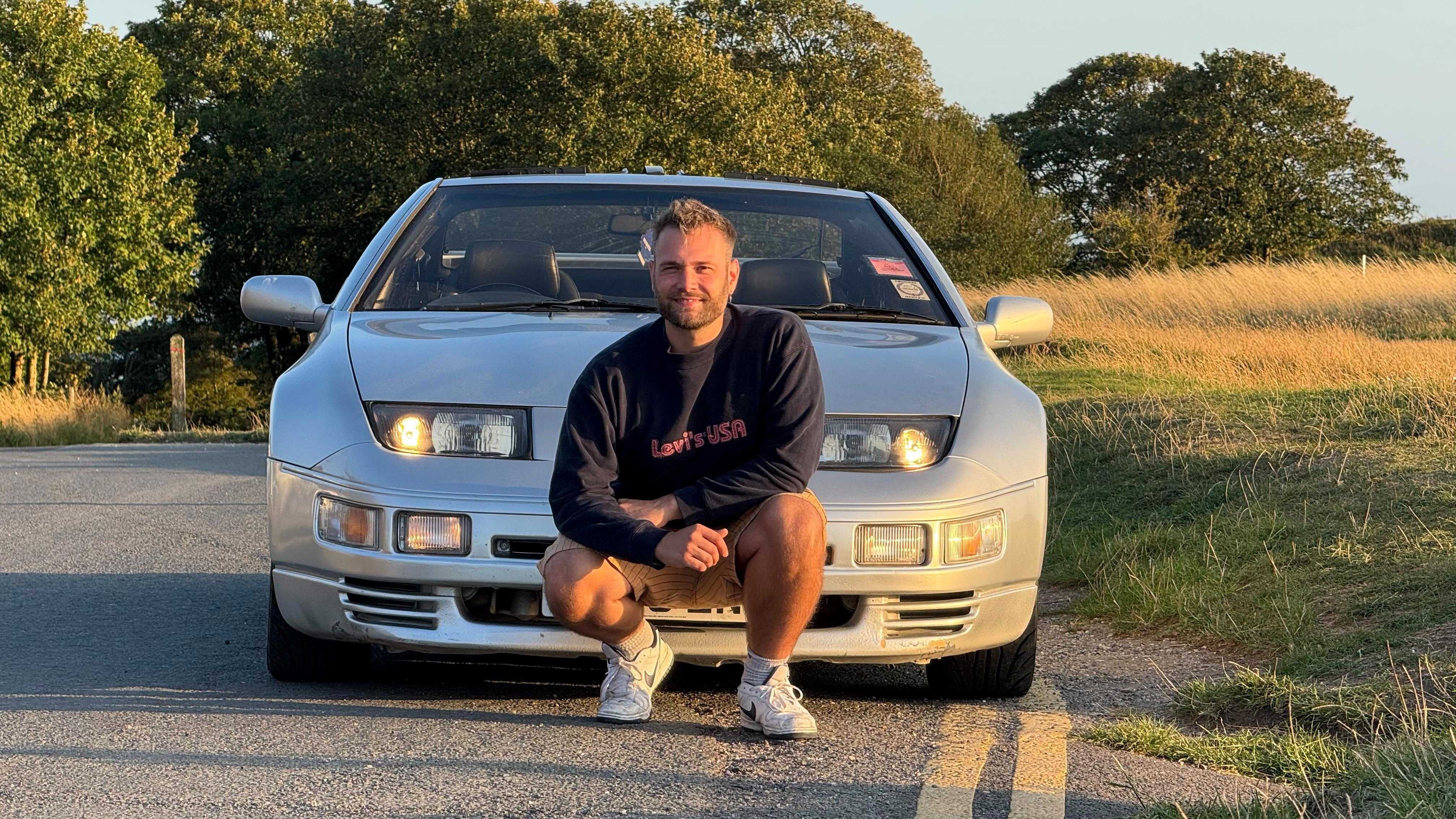 Author Charles Harvey kneeling in front of a car