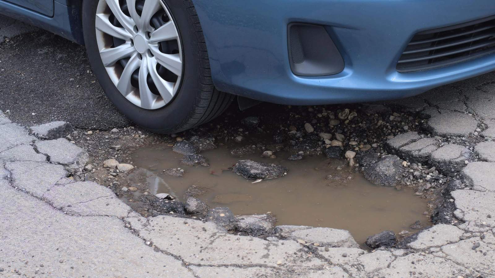 A blue car driving into a pothole filled with water
