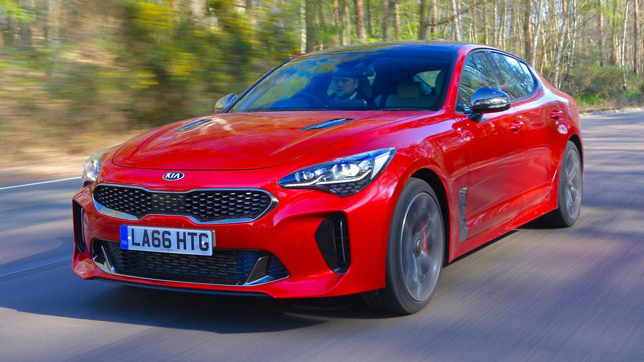 Kia Stinger driving on a UK B-road with trees in background