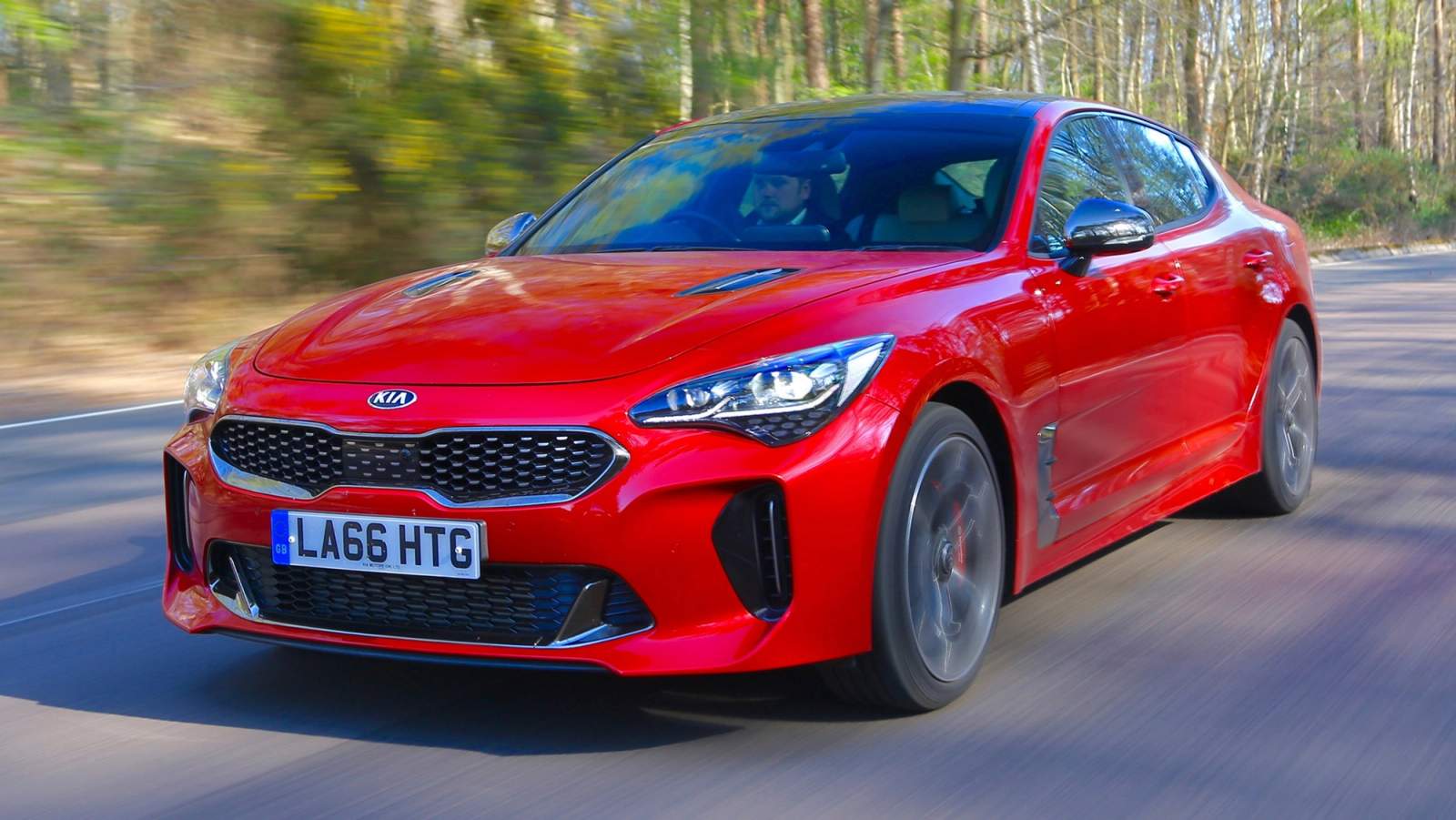 Kia Stinger driving on a UK B-road with trees in background
