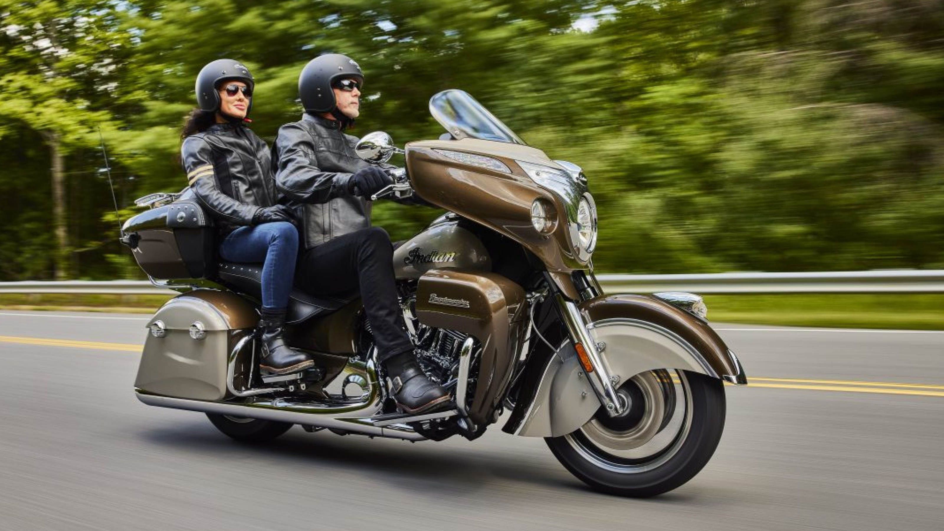 Two riders wearing leather jackets and helmets on a motorbike