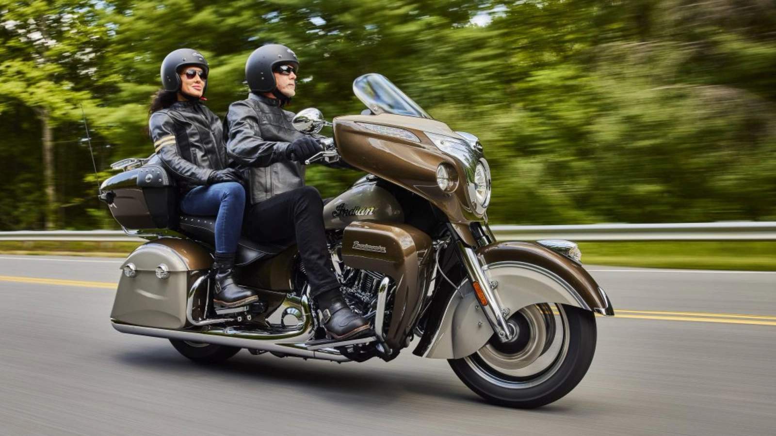 Two riders wearing leather jackets and helmets on a motorbike