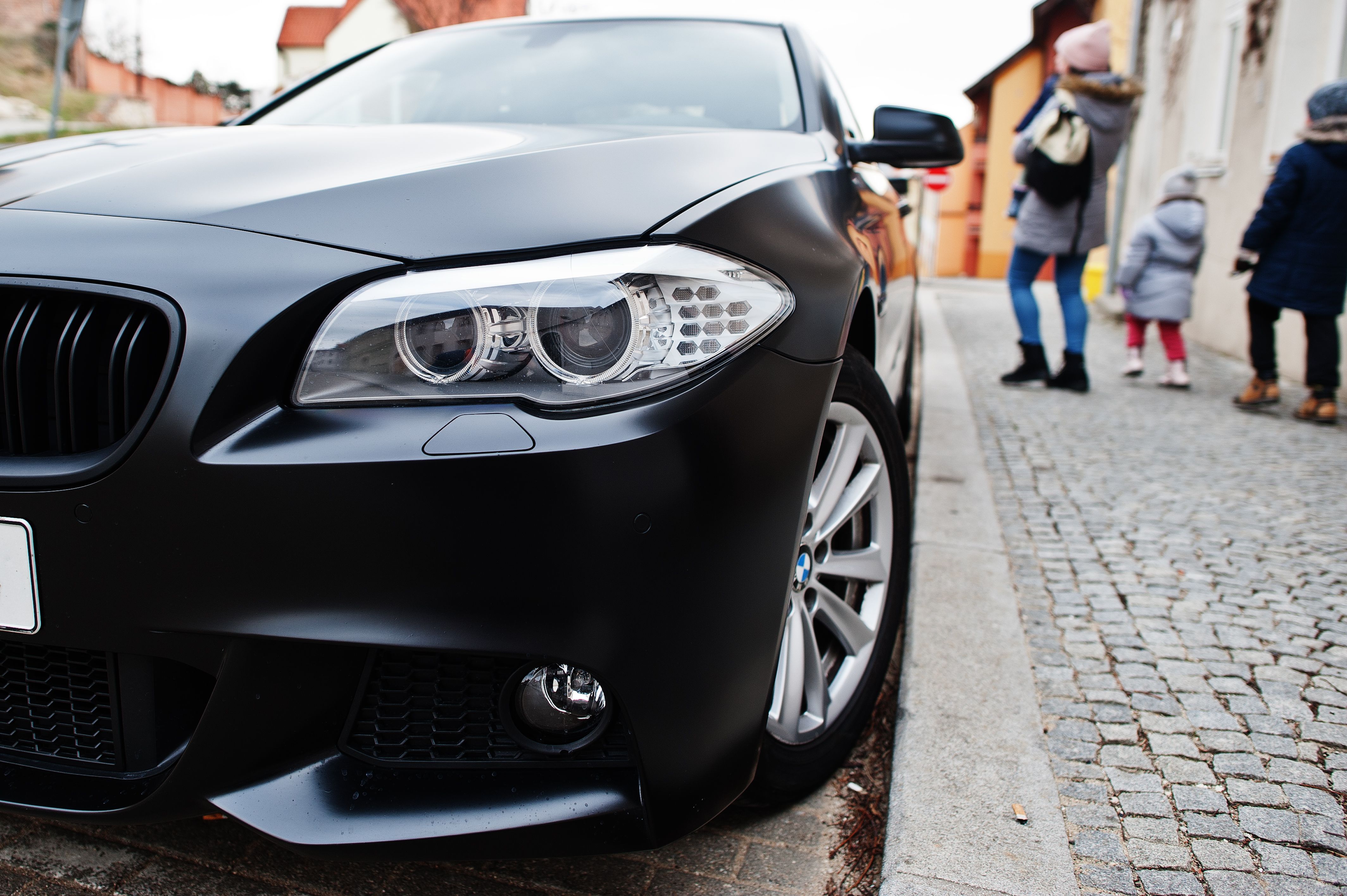 front of BMW parked on the street near family of three