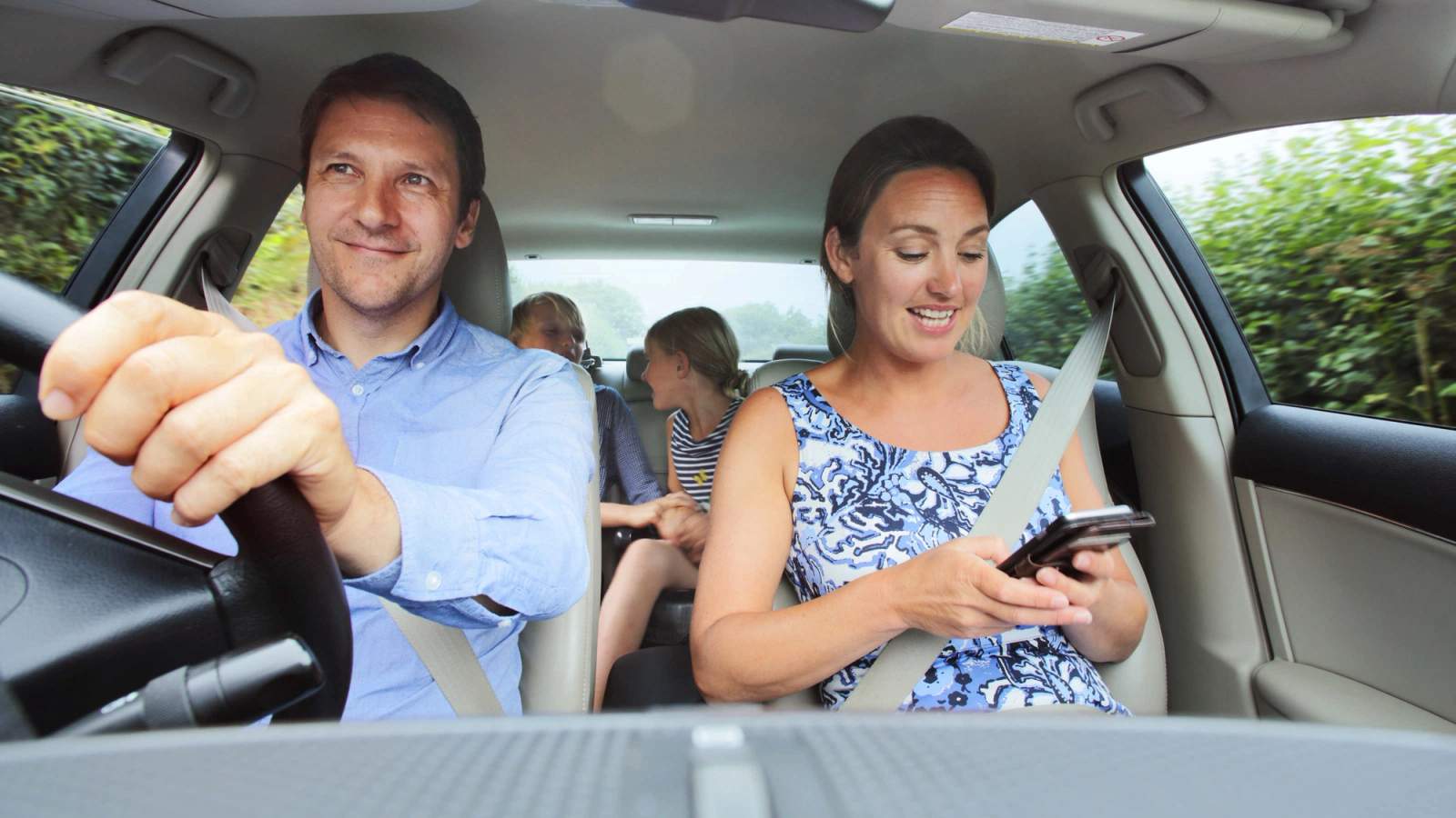 A family enjoying a trip in the car while the mum looks at her phone