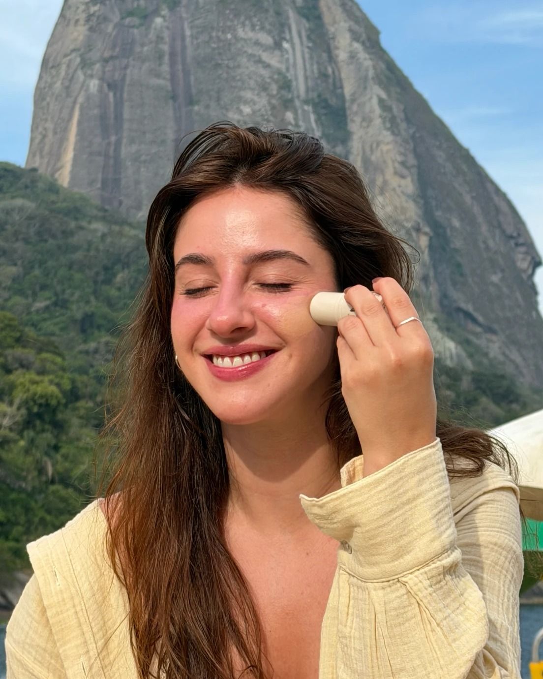 Modelo aplicando o blush stick ADCOS com o Pão de Açúcar ao fundo, no Rio de Janeiro