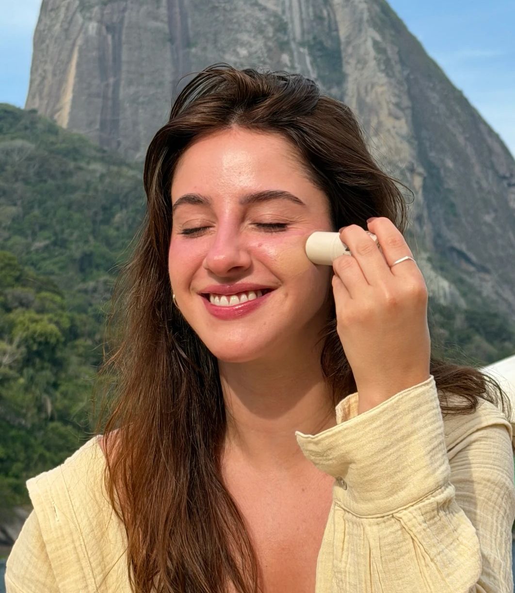 Modelo aplicando o blush stick ADCOS com o Pão de Açúcar ao fundo, no Rio de Janeiro