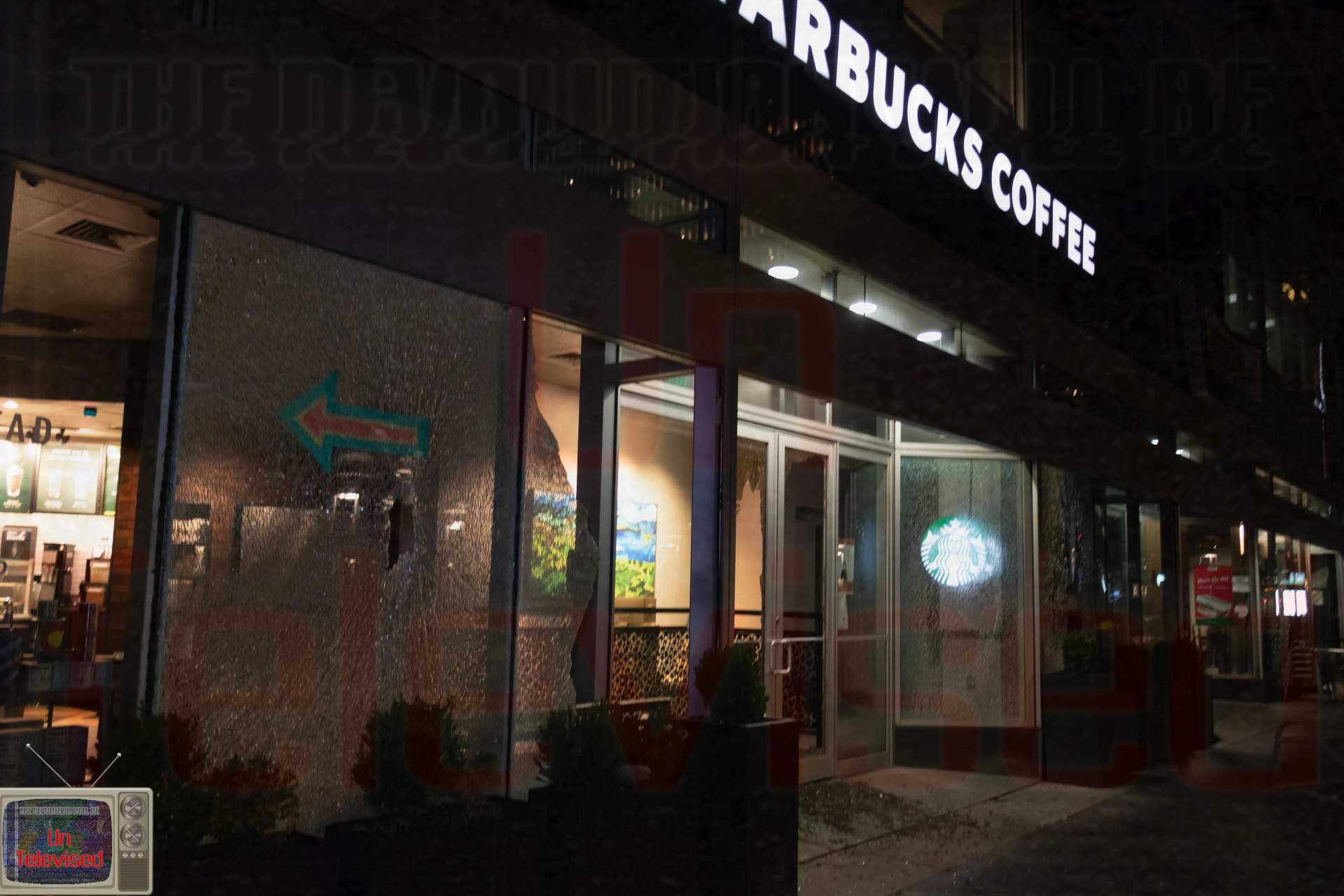 A Starbucks Coffee storefront with its large window shattered into a spiderweb pattern, the logo still glowing faintly inside.  [Radical Edward - Untelevised Media]
