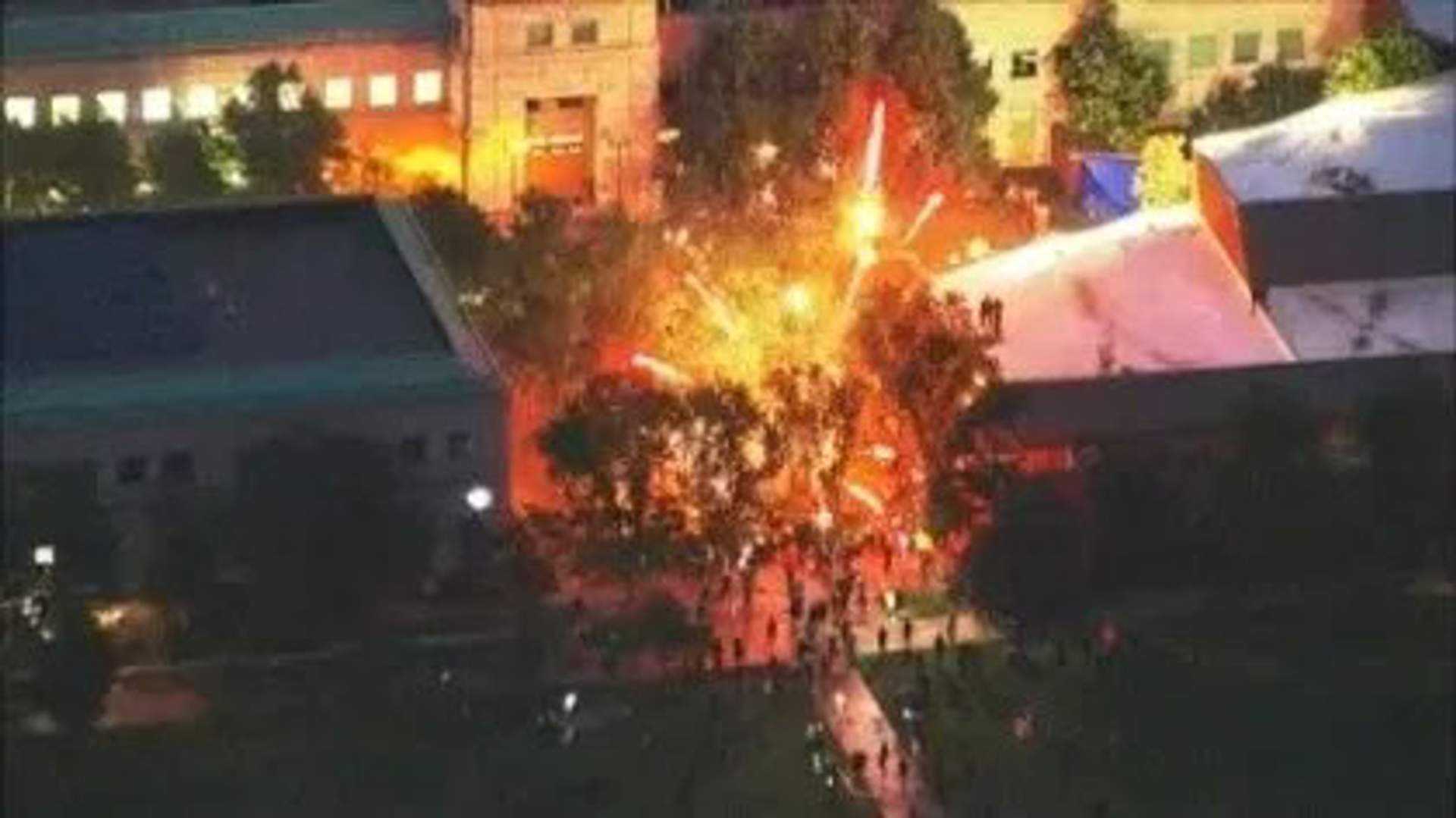 Mortar shell fireworks hitting police line behind fence at Aurora Courthouse. [Denver 7 Aerial Stream Screenshot]]