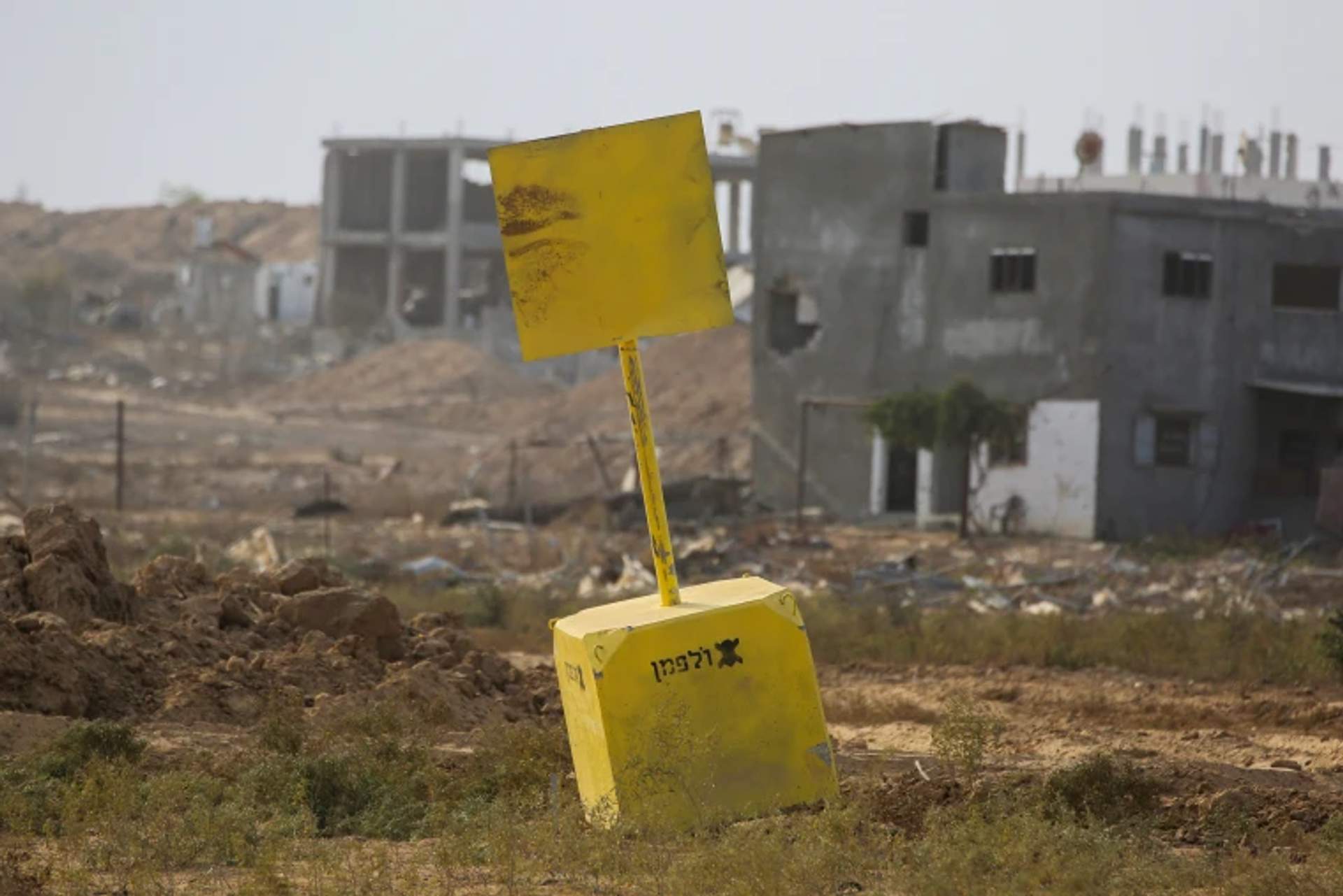 Concrete block marking the Yellow Line boundary in Gaza with open terrain and a military outpost visible in the background.