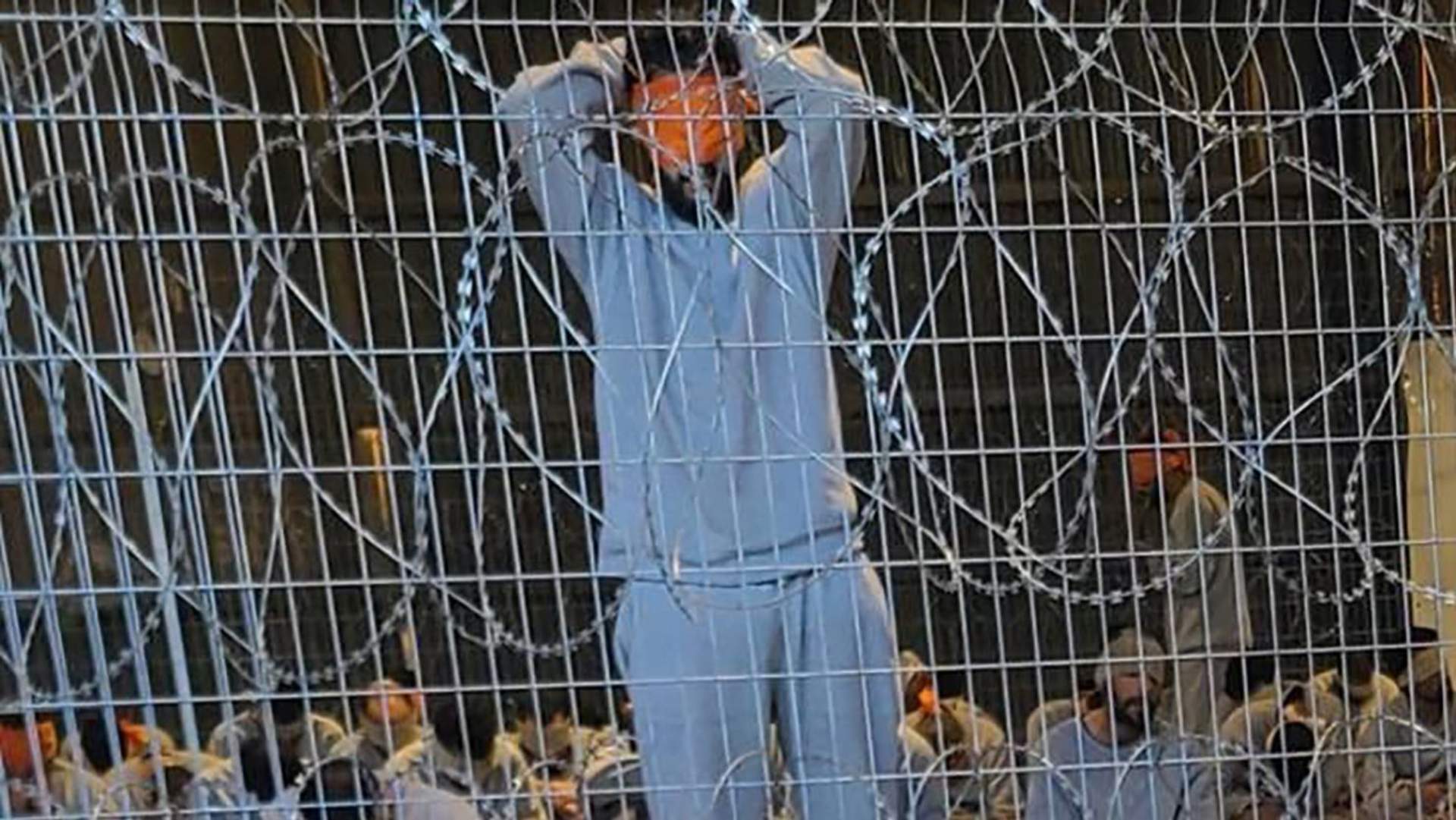 A prison stands blind folded against a razor wire fence in Sde Teiman