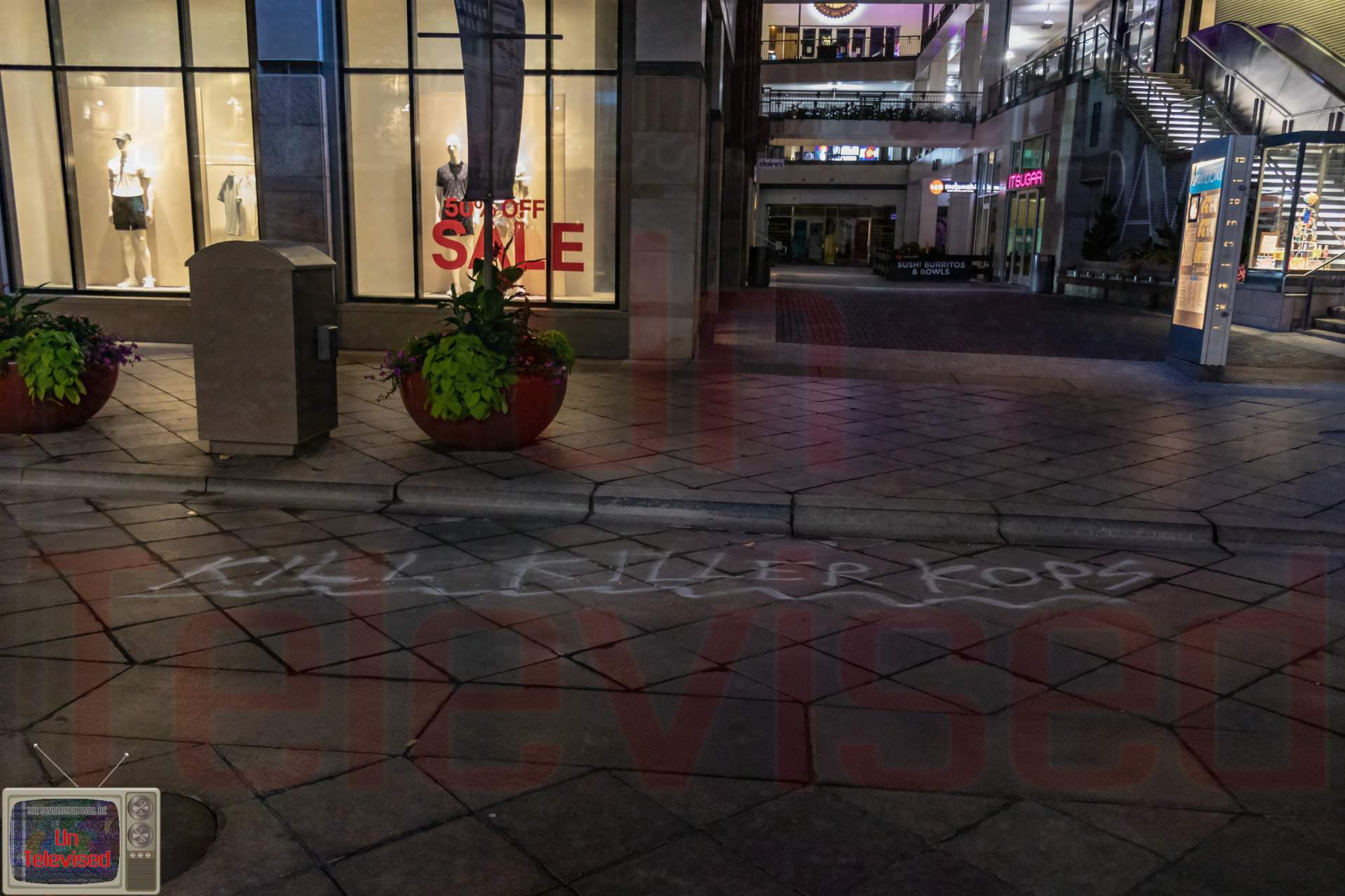 Sidewalk pavement near a retail storefront with "KILL KILLER KOPS" spray-painted in white chalk-like lettering. [Radical Edward - Untelevised Media]