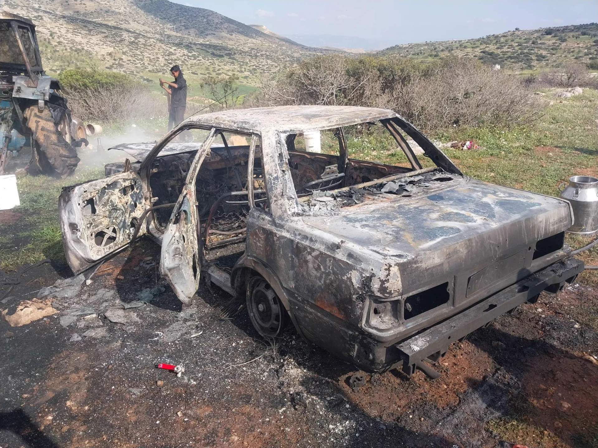  Palestinians stand near a vehicle destroyed in an Israeli settler attack in the West Bank