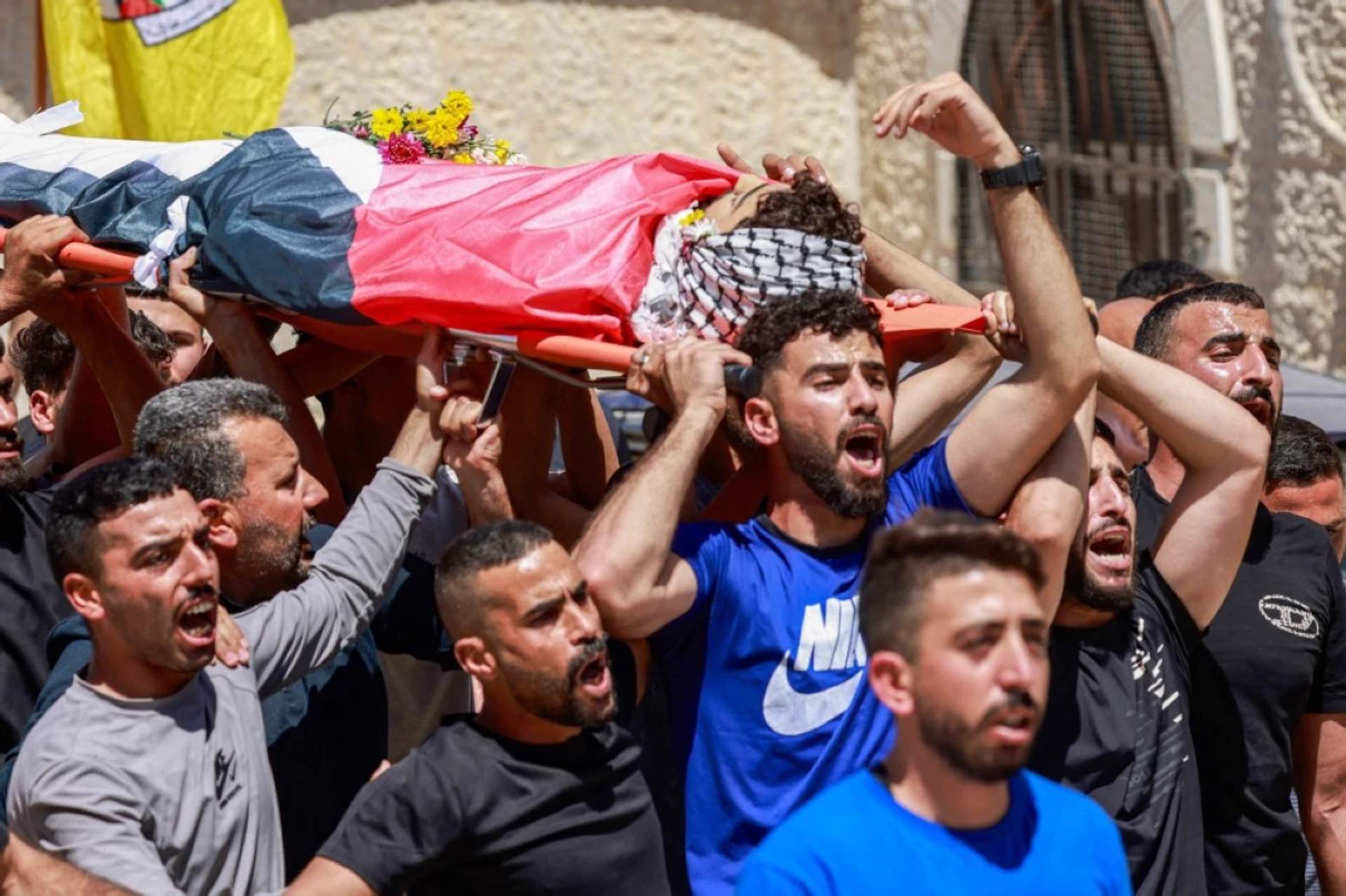 Palestinian men gathered around two bodies on stretchers during an outdoor funeral ceremony in Deir Jarir after a settler-military raid