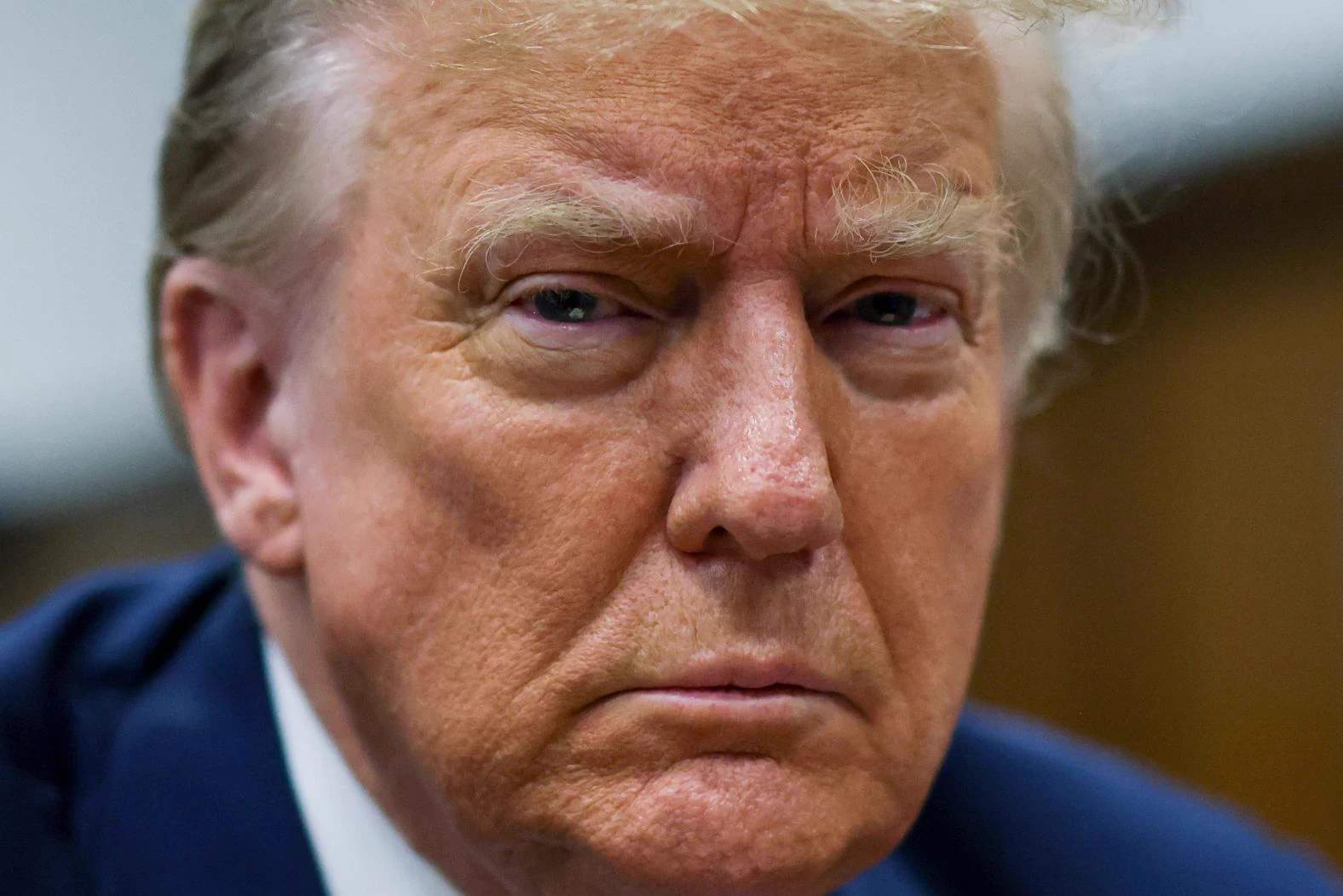 Donald Trump seated at a table inside a Manhattan courtroom surrounded by lawyers and security personnel during his hush money trial, April 2024