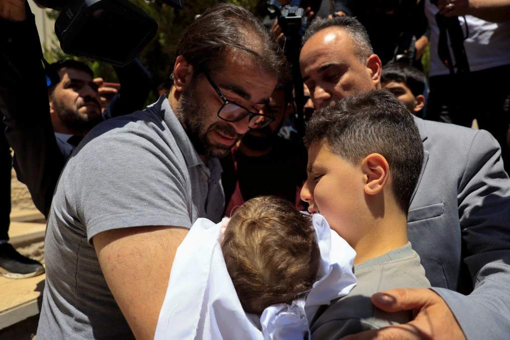 Large crowd of Palestinian men in funeral procession carrying a small body wrapped in a white shroud
