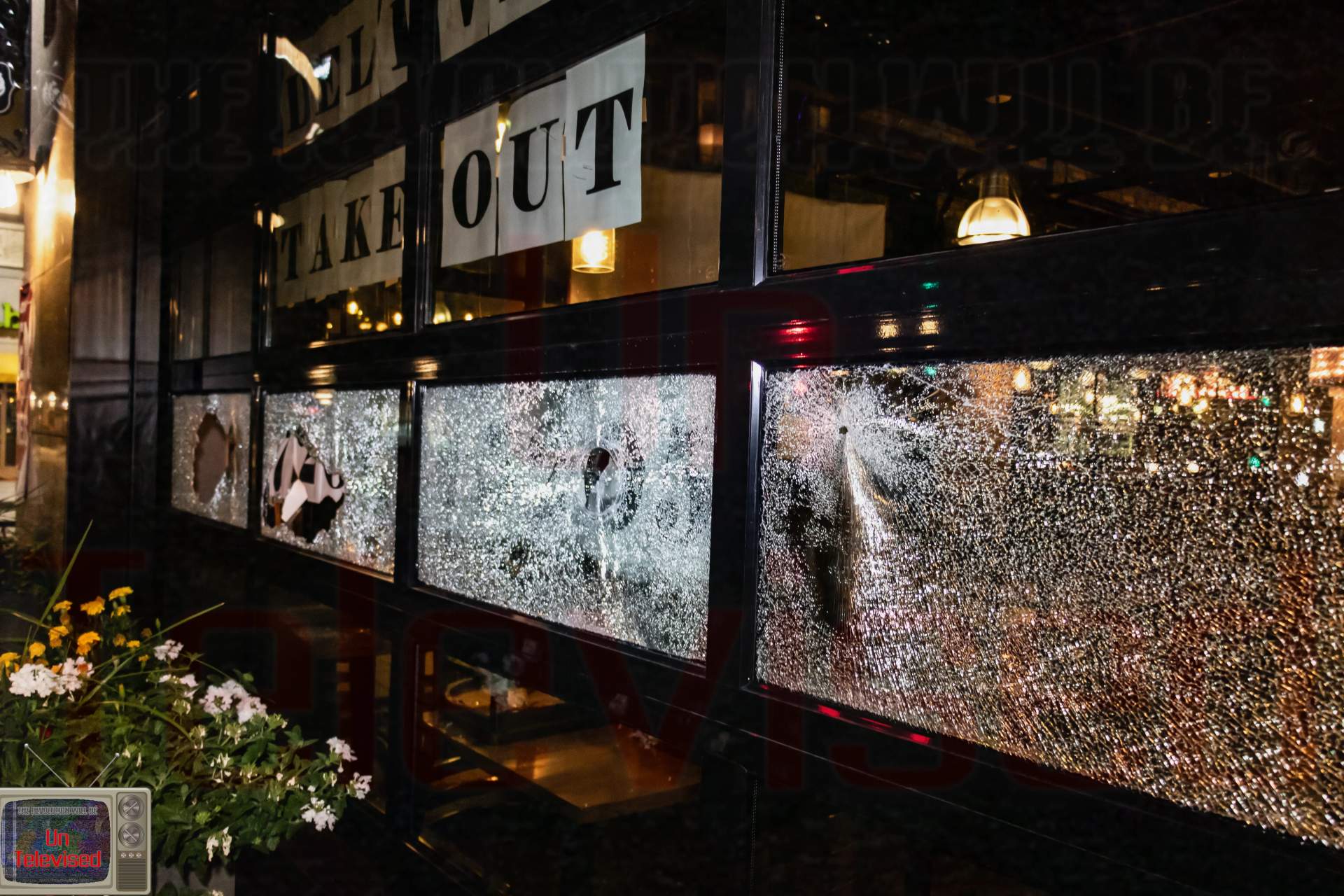 A row of restaurant windows with multiple shattered panels and punched-through holes beneath "Delivery/Takeout" signage. [Radical Edward - Untelevised Media]