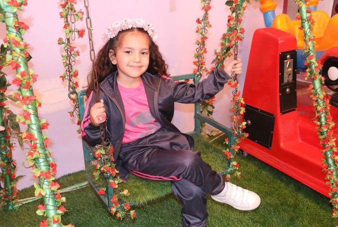 Hind Rajab on a playground swing, wearing a flower crown and smiling.