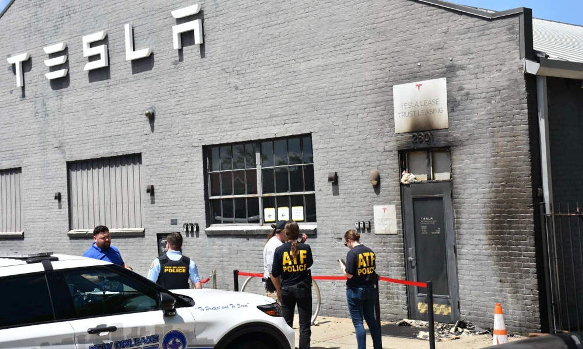 Scorched door of Tesla service center in New Orleans after Molotov cocktail attack on April 15, 2026. The door shows visible fire damage with soot and charring around the entryway.