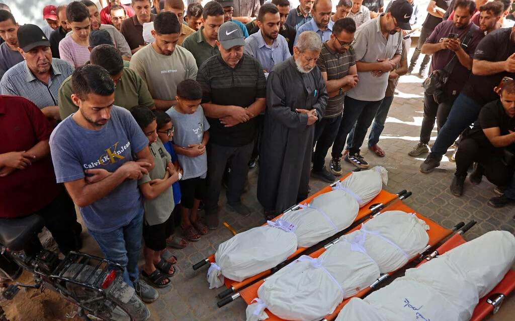 Palestinian men standing in a circle praying over shrouded bodies on the ground near damaged buildings after Israeli airstrikes in Gaza City on June 4, 2026