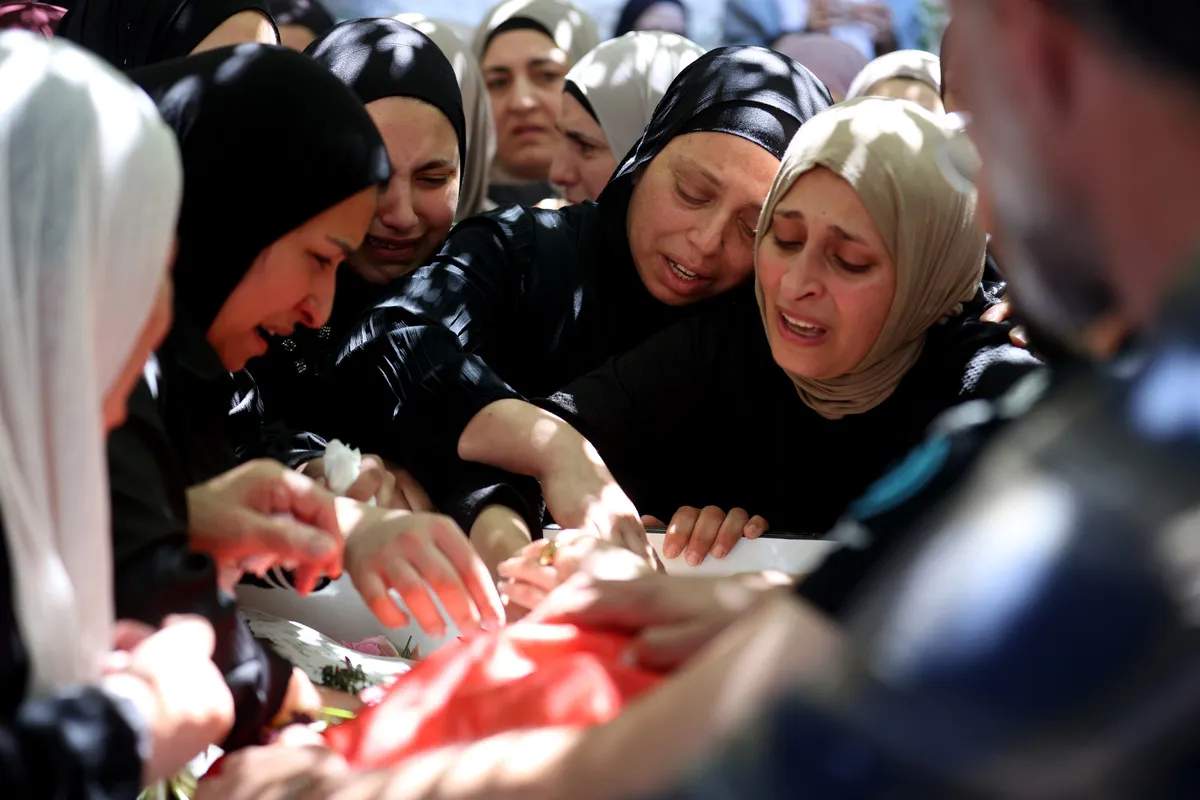 A woman in black bending over the shrouded body of 17-year-old Fadi al-Naasan on a stretcher, grieving at his funeral in al-Mughayyir