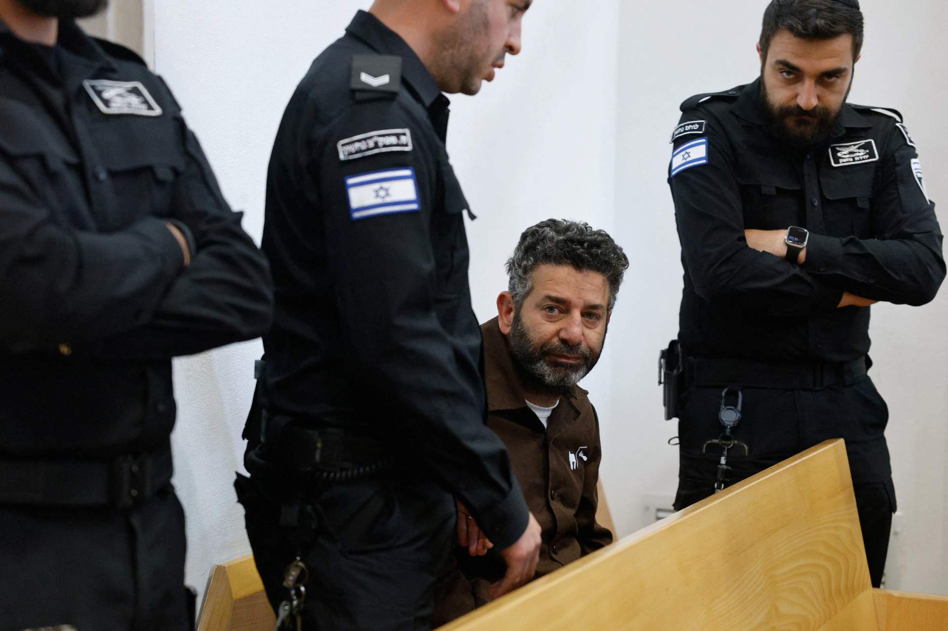 Saif Abu Keshek, in a white shirt and black pants, and Thiago Ávila, in a black t-shirt and jeans, walk alongside Israeli police officers outside a courthouse in Beersheba, Israel on May 5, 2026. Both activists were detained in international waters while participating in a humanitarian aid flotilla to Gaza.