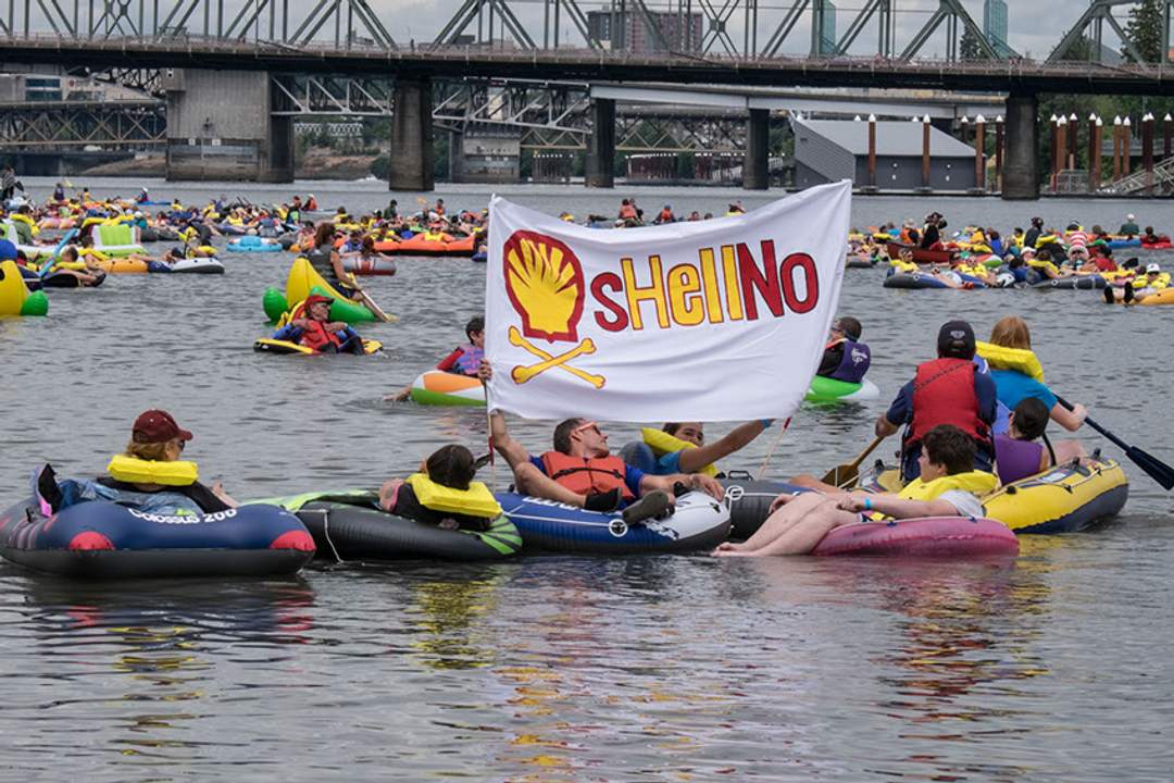 Activists in kayaks and inflatable rafts hold a banner reading 'sHellNo' beneath a bridge on the Willamette River in Portland.