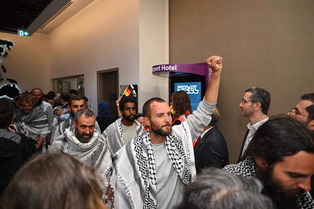 A crowd of flotilla activists waving Palestinian and other flags on a ship deck arriving in Istanbul after Israeli detention